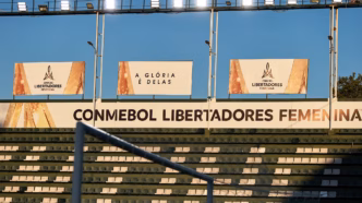 Jogadoras em campo durante a Libertadores Feminina na Argentina, com torcida ao fundo.