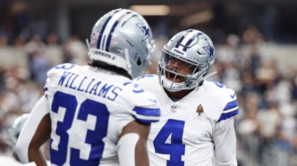 Javonte Williams correndo com a bola enquanto Dak Prescott observa em jogo do Dallas Cowboys.